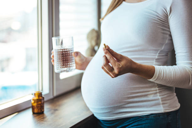 Female sitting at home in bed with glass of water medicine Pregnant woman reading label on bottle with medicine, with vitamins. Female sitting at home in bed with glass of water medicine. Pregnancy, health, pharmaceuticals, care and people. folic acid stock pictures, royalty-free photos & images