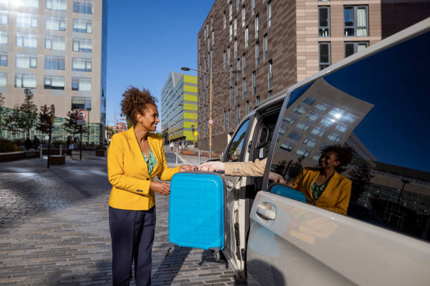 Ready To Go A close-up side view of a woman dressed in a bright yellow blazer handing her travel case to her colleague in the electric car they are being driven into their next meeting. They are in Newcastle upon Tyne in the North East of England. walking into glass door stock pictures, royalty-free photos & images