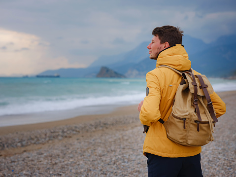 Handsome man in yellow jacket walking beach in antalya, turkey. Good looking male model looking pensive at ocean sea. Fantasy storytelling content