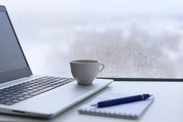 copo de café, laptop e bloco de notas com caneta em uma mesa contra a janela, vista para a cidade de inverno - heat snow urban scene creativity - fotografias e filmes do acervo