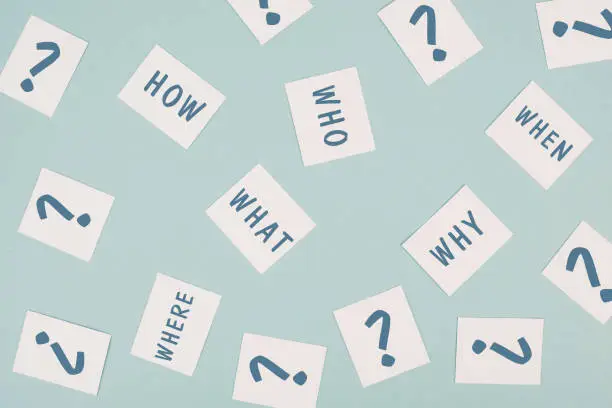 The words who what where how why and when are standing on small pieces of paper, question marks, asking for solution, problem solving