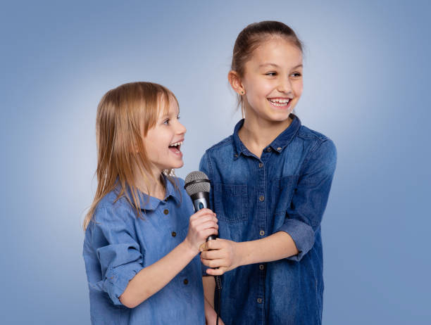 dos niñas de 6 y 8 años cantan una canción en un micrófono. el concepto es infancia, estilo de vida, música, canto, amistad sobre fondo azul - 8 9 years studio shot friendship sibling fotografías e imágenes de stock