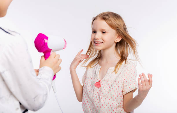 deux belles filles de 6 à 8 ans jouent avec le sèche-cheveux. les filles s’amusent à passer du temps ensemble et à sécher les cheveux sur fond blanc - female 8 9 years child excitement photos et images de collection