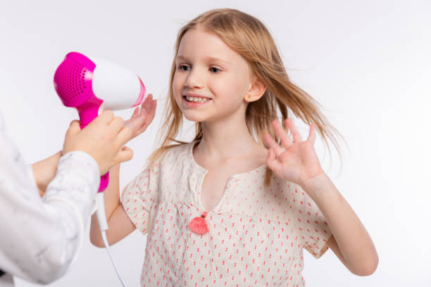 deux belles filles de 6-8 ans jouent avec le sèche-cheveux. les filles s’amusent à passer du temps ensemble et à sécher les cheveux sur fond blanc - female 8 9 years child excitement photos et images de collection