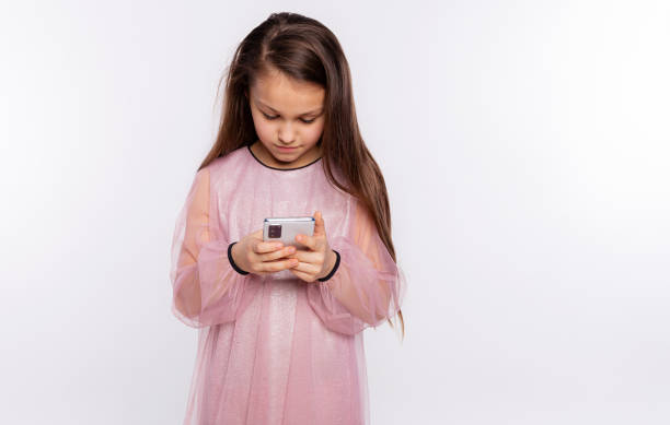 kaukasisches kindermädchen schaut auf den bildschirm des mobiltelefons, das video ansieht oder text eintippt, isoliert über weißen hintergrund freien raum für ihren text - telephone child isolated on white elegance stock-fotos und bilder