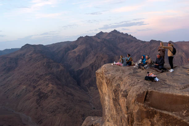 les touristes s’assoient au bord d’une falaise et regardent le lever du soleil. trekking au mont moïse. péninsule du sinaï en égypte. - sinai peninsula photos et images de collection