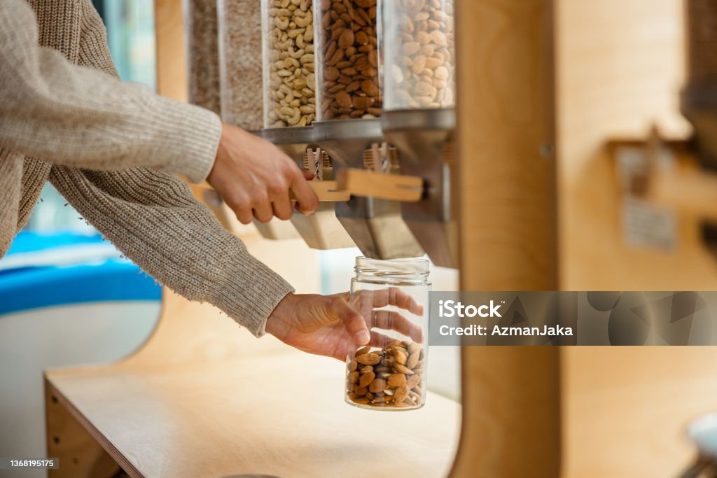 Close Up Of A Female Using A Nuts Dispenser In A Zero Waste Store Close up of a female costumer using a grains or cereal dispenser in a zero waste shop. Refill Stock Photo