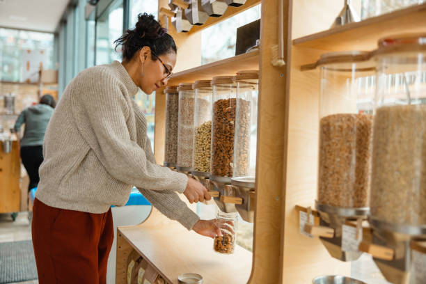 Female Using A Nuts Dispenser In A Zero Waste Store Female costumer using a grains or cereal dispenser in a zero waste shop. sustainable business stock pictures, royalty-free photos & images