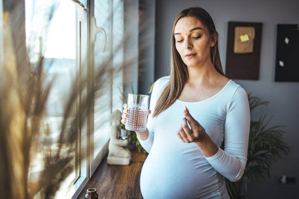 une femme heureuse tient un verre d’eau, prend quotidiennement de la vitamine d - human pregnancy abdomen human skin healthcare and medicine photos et images de collection