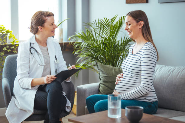The woman is holding her stomach while the doctor writes information on a clipboard. A pregnant woman and her doctor are indoors in a medical center. The woman is holding her stomach while the doctor writes information on a clipboard. gynecological examination photos stock pictures, royalty-free photos & images