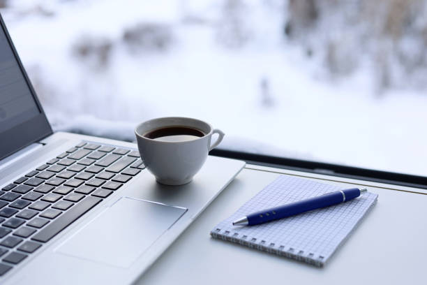 laptop, xícara de café e bloco de notas com caneta em uma mesa contra a janela, vista para a cidade de inverno - heat snow urban scene creativity - fotografias e filmes do acervo