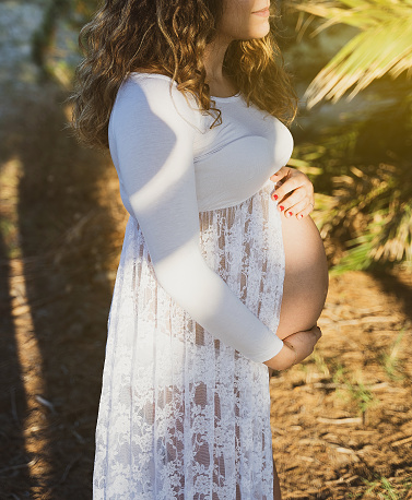 Maternity concept. Pregnant woman with white dress holding her belly at sunset