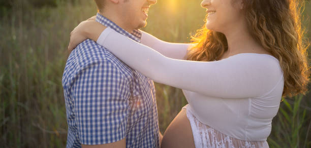 un jeune couple enceinte s’embrasse et sourit dans la forêt au coucher du soleil - boyfriend heterosexual couple married human pregnancy photos et images de collection
