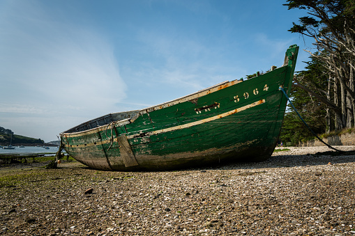 Lanilis, France - August 10, 2020: Old green boat lying on the beach, low tide, sunny day in summer