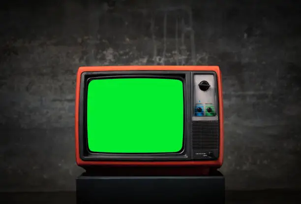 Photo of Retro old TV with green screen on wooden box in front of old wall background.