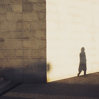 A woman strolls in Marseille at sunset and her shadow is reflected on the harbor wall