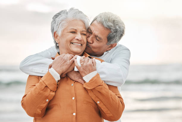 plan recadré d’un couple de personnes âgées affectueux partageant un moment intime sur la plage - retirement beach women vacations photos et images de collection
