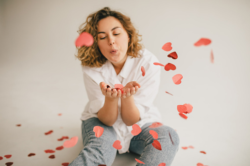 Happy millennial woman with red heart cofetti on white background. Saint Valentine's Day celebration.