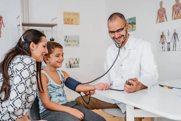 Young male pediatrician measuring blood pressure of a child patient.