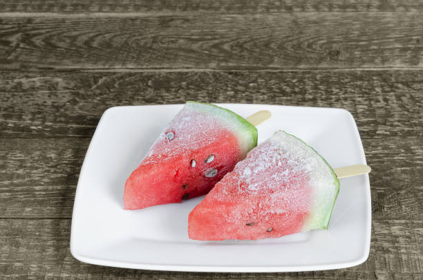 Frozen watermelon fruit desserts on a stick, in a plate on an old wooden background. Selective focus stock photo