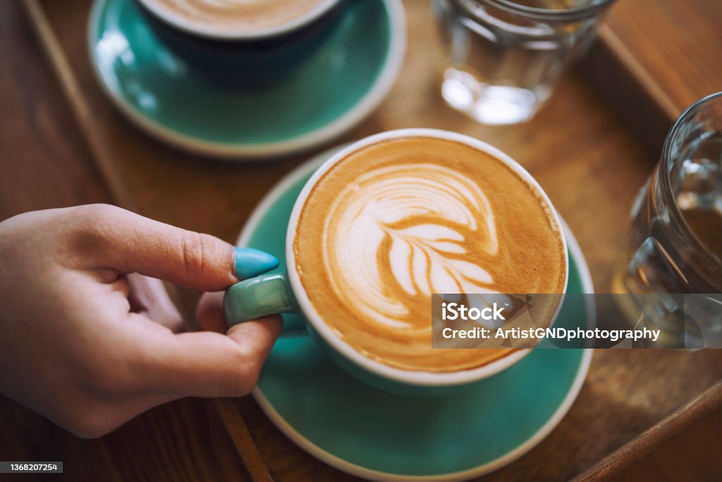Woman holding a cup of cafe latte in cafe. Shot of unrecognisable woman holding a cup of cafe latte in cafe. Latte Stock Photo