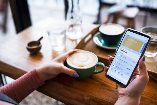 Photo of Shot of young woman managing bank account on smartphone at cafe.