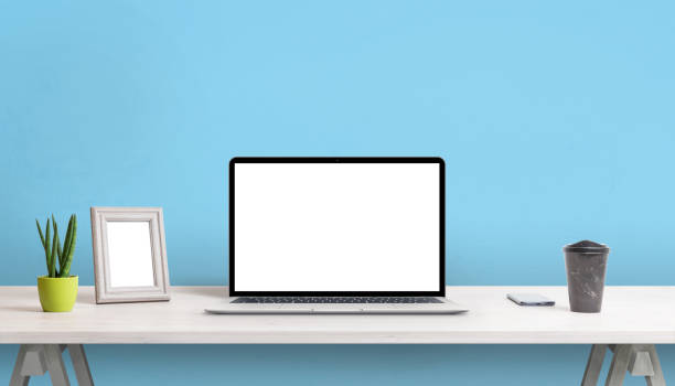 istock Laptop with blank screen on work desk. Picture frame, plant, coffee and phone beside. Blue wall in background 1368207634