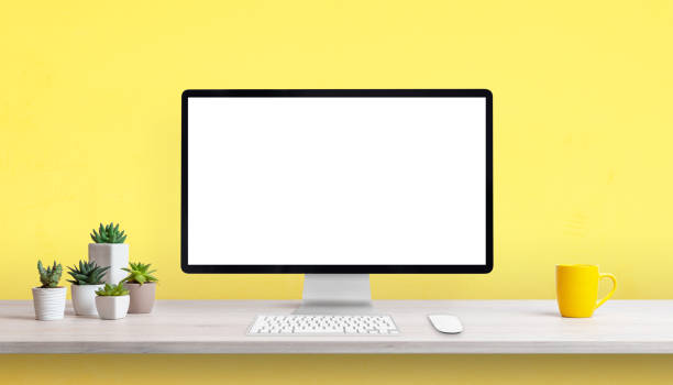 istock Creative work desk with blank computer display, yellow coffee mug and plants. Yellow background with copy space 1368207635