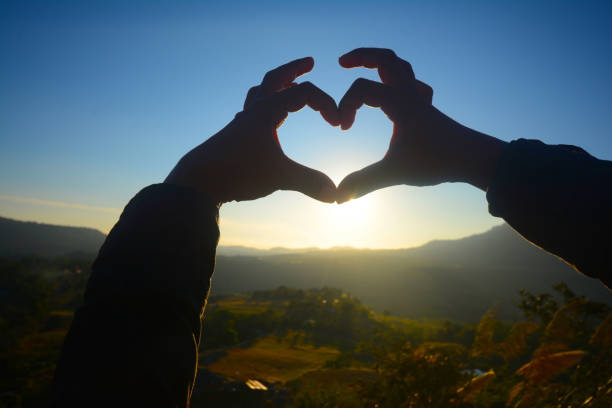 istock Hands making heart shape on sunrise over mountains. 1368215775