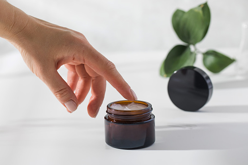 A woman's hand reaches for a jar of nourishing skin cream on a white background with a shadow pattern. High quality photo