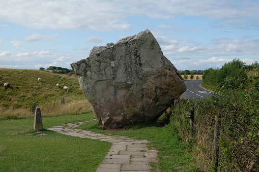 giant square rock in a meadow with sheep in england