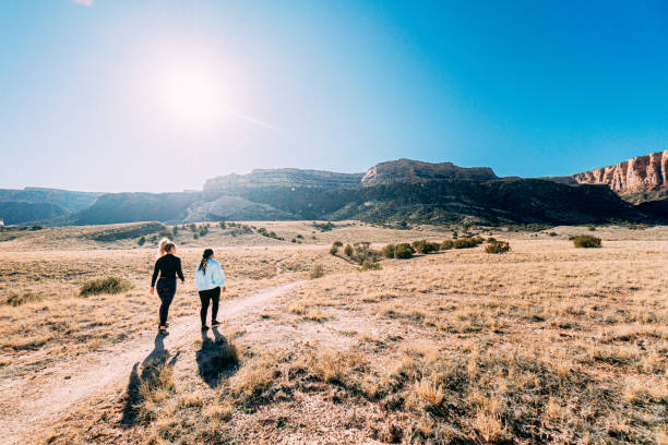 wide angle shot of two young women outdoors getting some exercise together in a desert recreational area on a hiking trailpath near the colorado national monument in grand junction - journey footpath exercising effort - fotografias e filmes do acervo