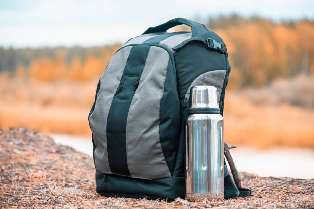 istock Hiking backpack with thermos for tea on the river bank. 1368220785