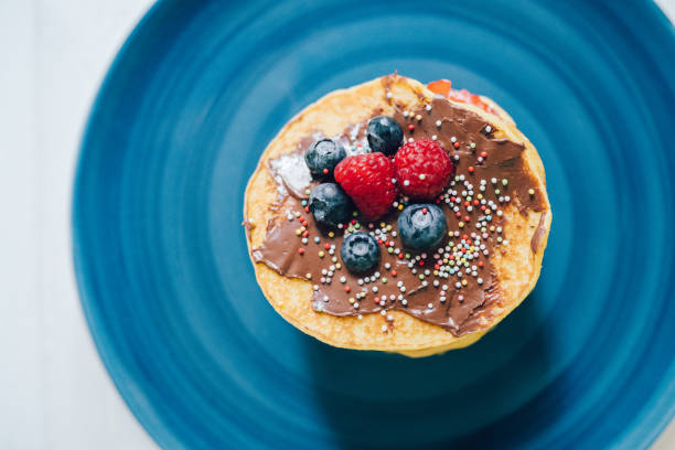 Pancakes with berries and chocolate cream on a blue plate. Brightly background.