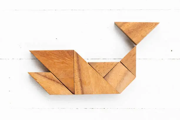 Photo of Wood tangram puzzle in whale, fish or shark shape on white wood background