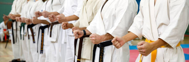 mestre de karatê em um quimono branco e com faixa preta, fica na frente da formação de seus alunos. escola de artes marciais em treinamento no ginásio - karate child judo belt - fotografias e filmes do acervo