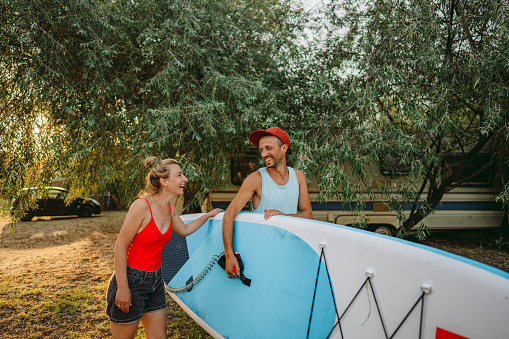 Photo of a happy couple carrying a paddleboard