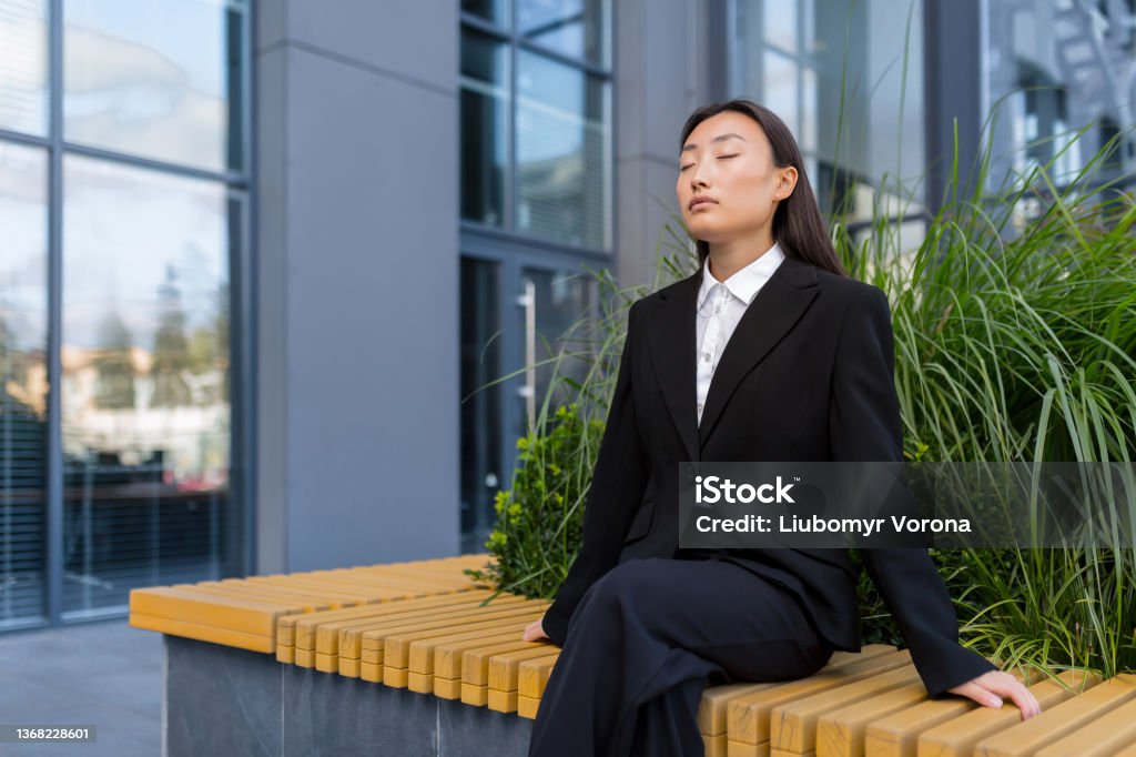 Beautiful Asian business woman sitting on a bench relaxing, meditating and performing breathing exercises Mindfulness Stock Photo