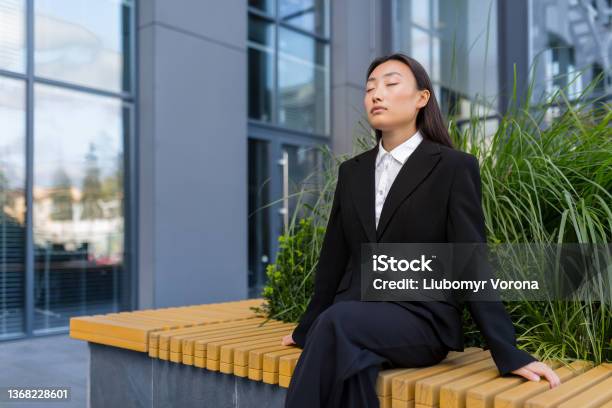 Beautiful Asian Business Woman Sitting On A Bench Relaxing Meditating And Performing Breathing Exercises Stock Photo - Download Image Now