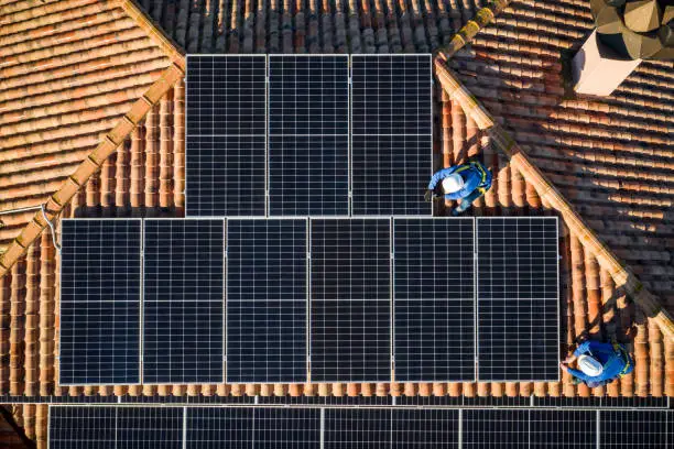 Photo of aerial view of Two workers installing solar panels on a rooftop