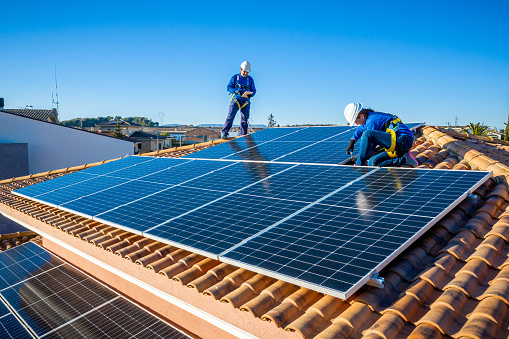kneeling professional workers fixing solar panels from the top of a house roof, side view of the roof with reflection