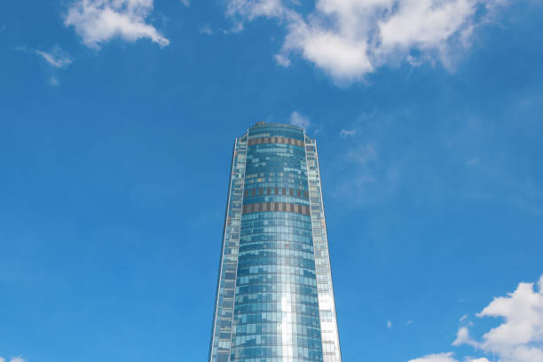 istock One multi-storey high mirrored shiny skyscraper against a blue sky with clouds. Bottom view 1368231857