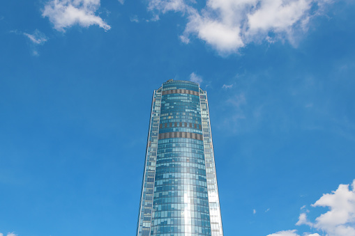 One multi-storey high mirrored shiny skyscraper against a blue sky with clouds. Bottom view.