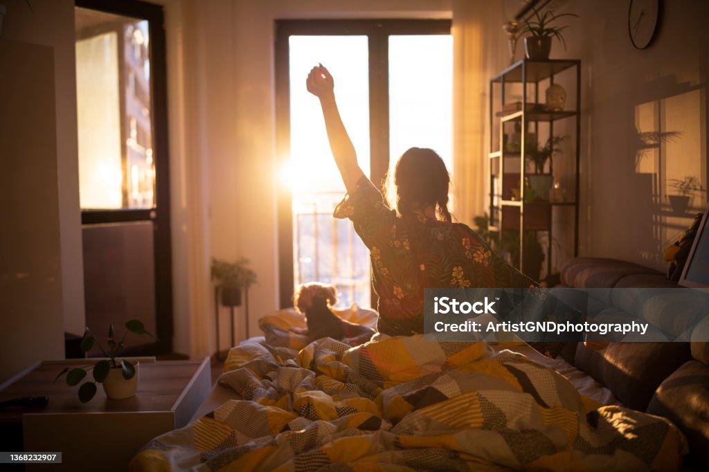 Waking up with the sun. Young woman streching in bed in the morning while looking at the sunrise. Waking up Stock Photo
