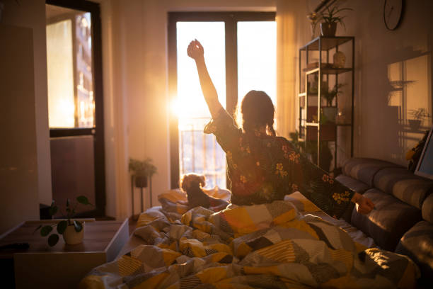 Waking up with the sun. Young woman streching in bed in the morning while looking at the sunrise. waking up stock pictures, royalty-free photos & images