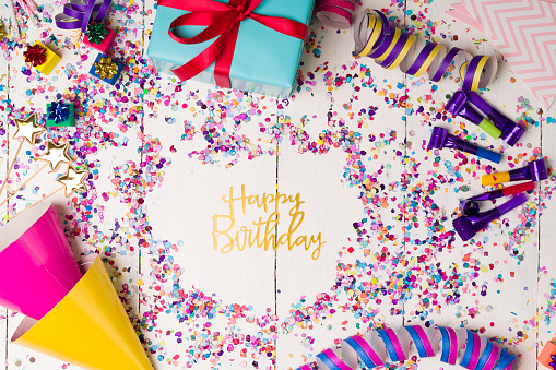 Wear a party hat. Party items to celebrate a birthday with a lot of confetti, serpentines and party whistlers next to presents