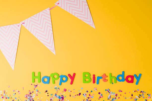 Studio shot of a colorful happy birthday with confetti and party items against a bright yellow background