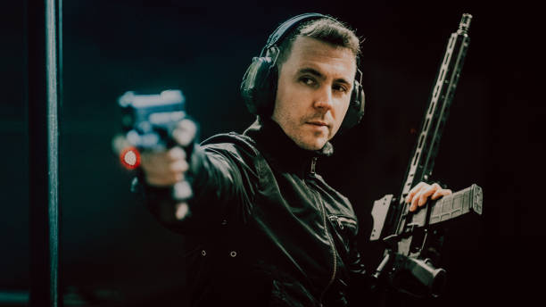 istock Professonal shooter aiming towards camera. Holding Glock 17 gun, wearing leather jacket and soundproof headphones 1368234594