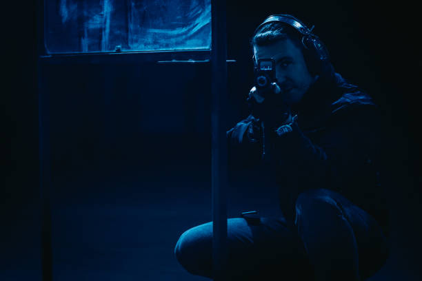 istock Man aiming M4 AR-15 rifle  towards camera in a dark, foggy shooting range. Blue light 1368235577
