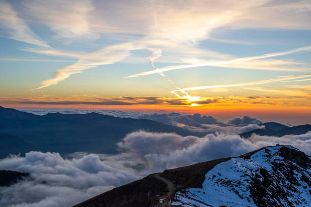 istock Snowy high mountains through the clouds in sunset sky 1368236324